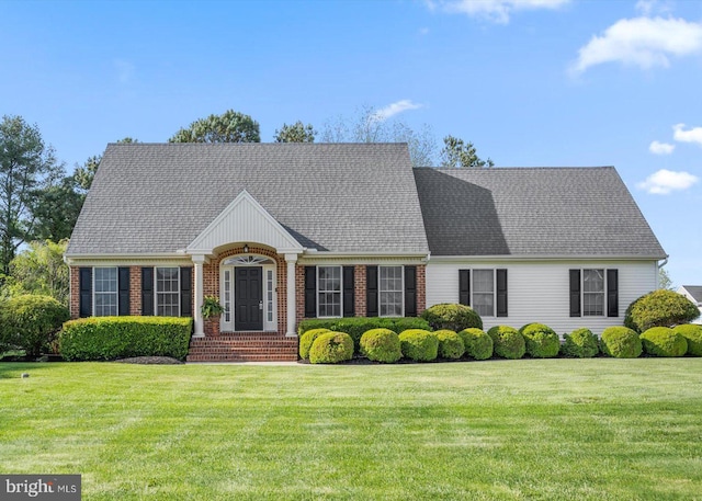 new england style home featuring a shingled roof, brick siding, and a front yard