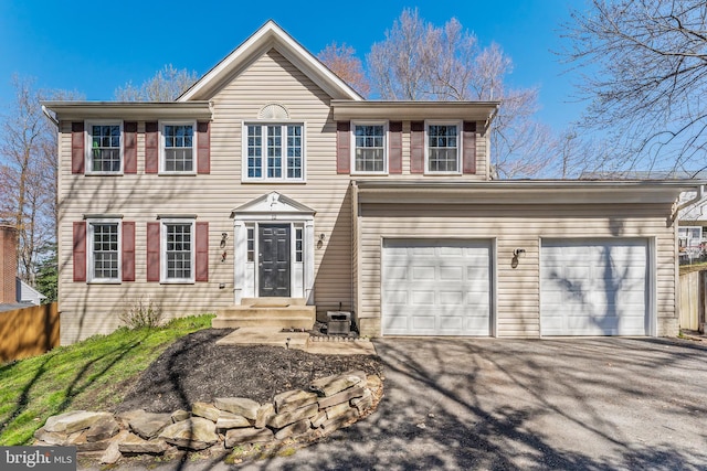 colonial home with an attached garage, fence, and aphalt driveway