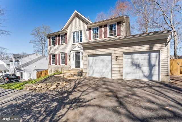 colonial-style house featuring a garage, driveway, central air condition unit, and fence