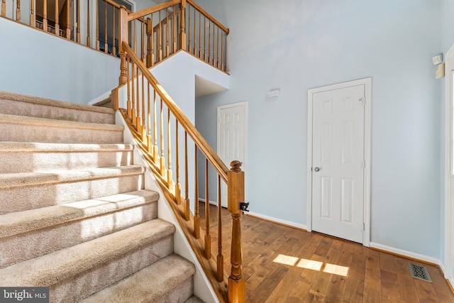 stairway with baseboards, visible vents, a high ceiling, and hardwood / wood-style flooring