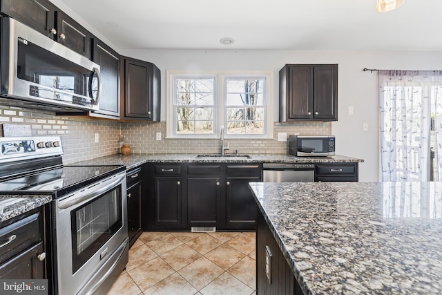 kitchen with dark stone counters, a sink, stainless steel appliances, and backsplash