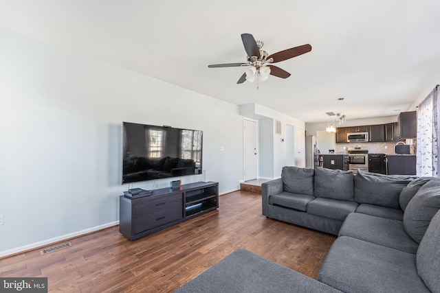 living room with dark wood-style floors, visible vents, baseboards, and ceiling fan with notable chandelier