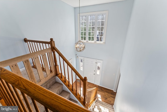 stairway with baseboards, wood finished floors, and a chandelier