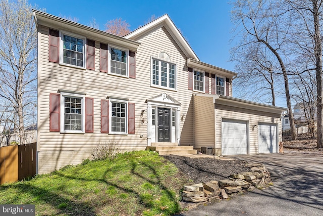 colonial house featuring driveway, an attached garage, and fence
