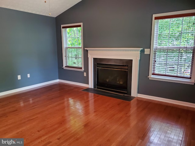 unfurnished living room featuring a fireplace with flush hearth, baseboards, lofted ceiling, and wood finished floors