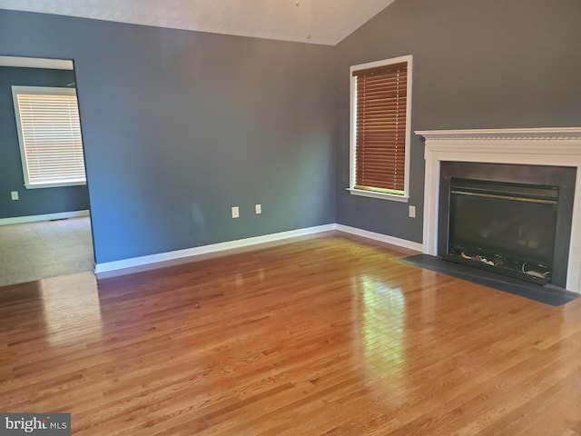 unfurnished living room featuring baseboards, a fireplace with flush hearth, wood finished floors, and vaulted ceiling