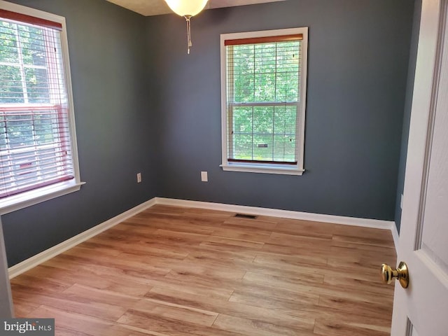 spare room featuring plenty of natural light, baseboards, light wood finished floors, and visible vents