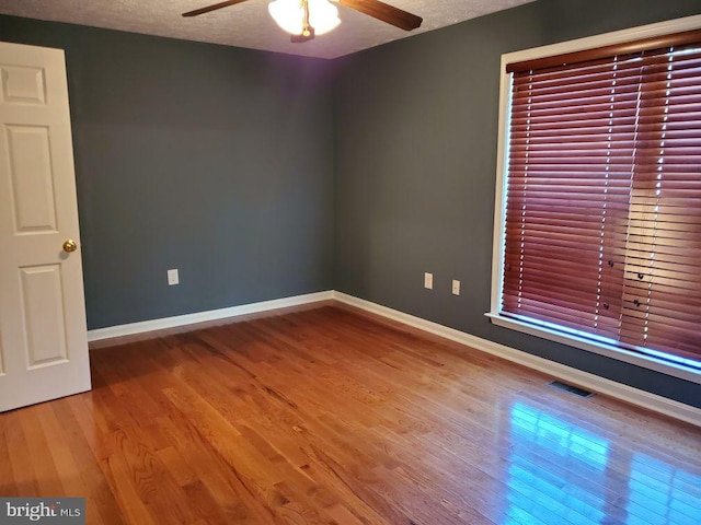 unfurnished room with baseboards, wood finished floors, ceiling fan, and a textured ceiling