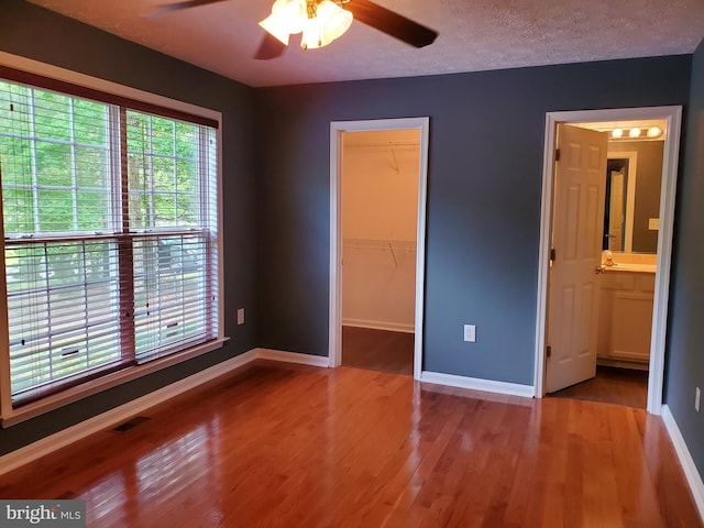 unfurnished bedroom with a spacious closet, baseboards, a textured ceiling, visible vents, and wood finished floors