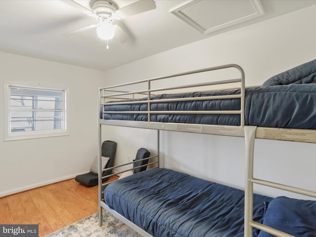 bedroom with baseboards, a ceiling fan, attic access, and wood finished floors