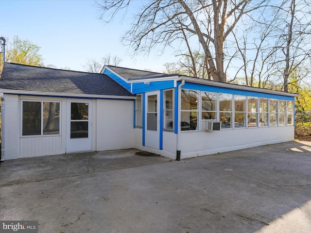 rear view of house featuring a patio area, concrete block siding, and a sunroom