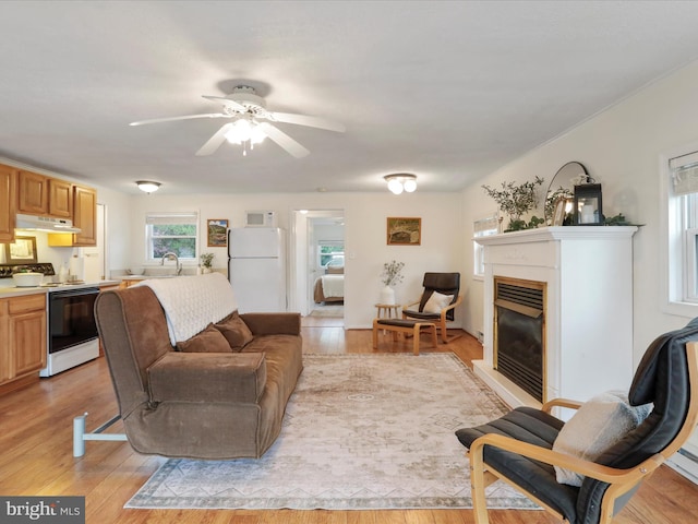living room featuring light wood-type flooring, a glass covered fireplace, and a ceiling fan