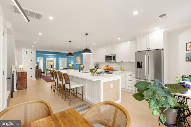 632 Rock Creek Church Rd NW Unit 2, Washington, DC 20010 - kitchen featuring appliances with stainless steel finishes, an island with sink, white cabinets, backsplash, and a kitchen breakfast bar