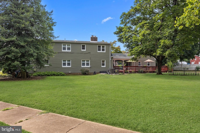 rear view of house with a chimney, fence, and a lawn