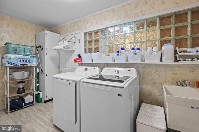 laundry room with laundry area, light wood-style flooring, washing machine and clothes dryer, a sink, and wallpapered walls