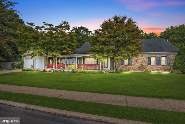 ranch-style home with covered porch, roof with shingles, stone siding, a front lawn, and driveway