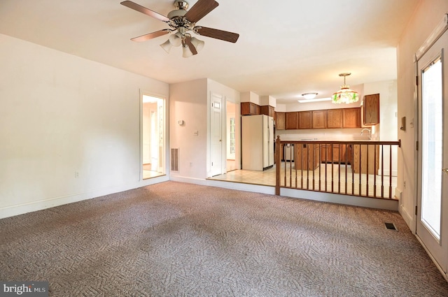 unfurnished living room with light colored carpet, baseboards, ceiling fan, and a sink