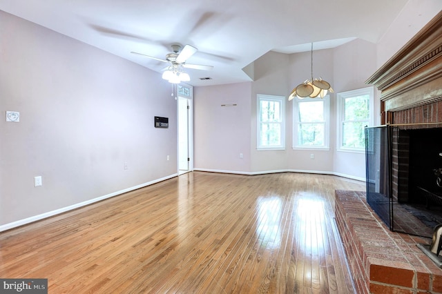 unfurnished living room featuring wood-type flooring, a brick fireplace, ceiling fan, and baseboards