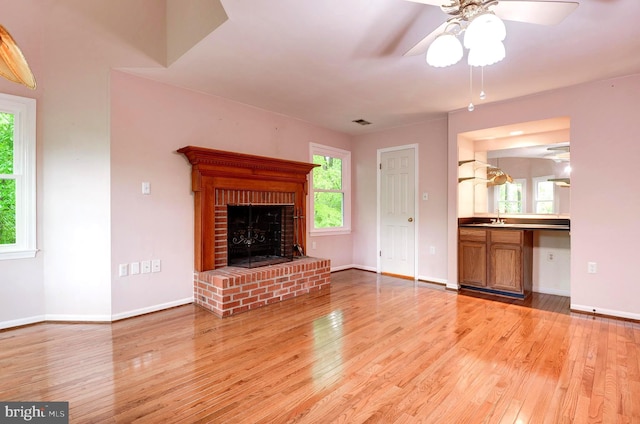 unfurnished living room featuring light wood-type flooring, a ceiling fan, a sink, a fireplace, and baseboards
