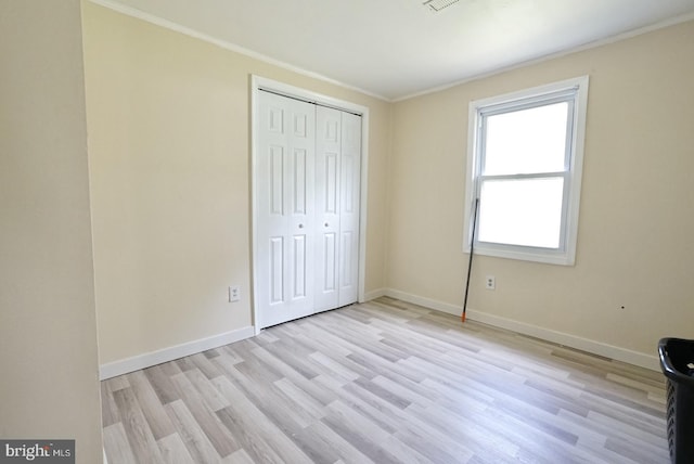 unfurnished bedroom featuring baseboards, crown molding, a closet, and light wood-type flooring