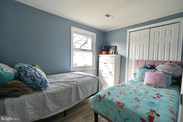 bedroom featuring visible vents, a closet, wood finished floors, and ornamental molding