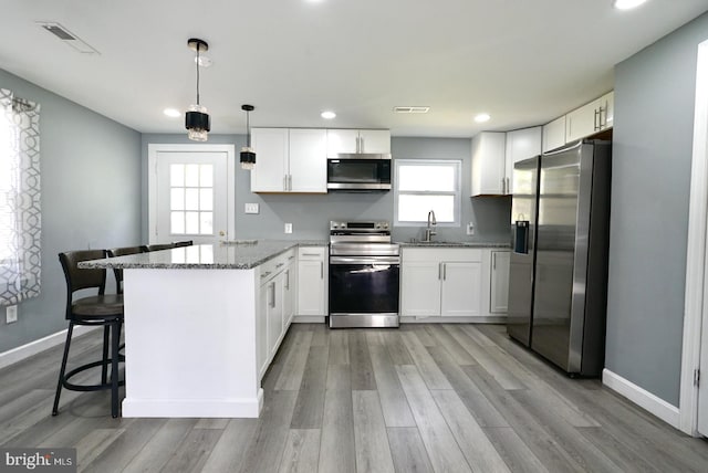 kitchen featuring light stone countertops, a sink, white cabinets, a peninsula, and appliances with stainless steel finishes