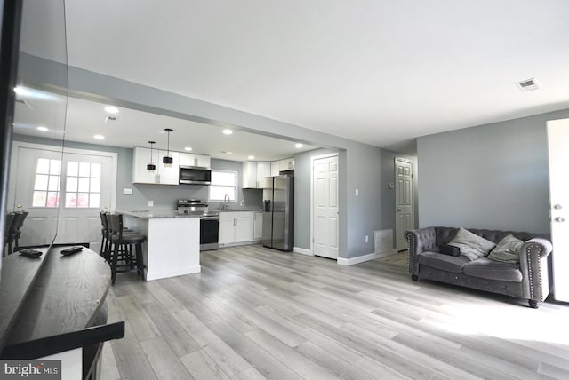 kitchen with white cabinetry, appliances with stainless steel finishes, open floor plan, light wood-type flooring, and visible vents