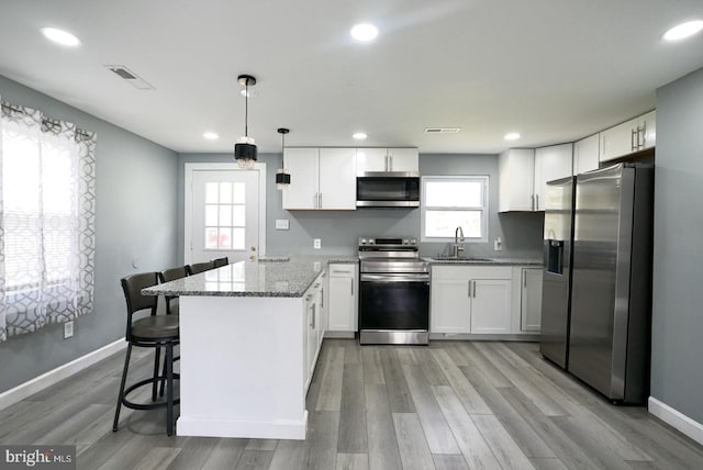 kitchen featuring light stone counters, a sink, appliances with stainless steel finishes, a peninsula, and white cabinets