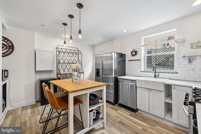 kitchen with light wood finished floors, a sink, backsplash, and appliances with stainless steel finishes