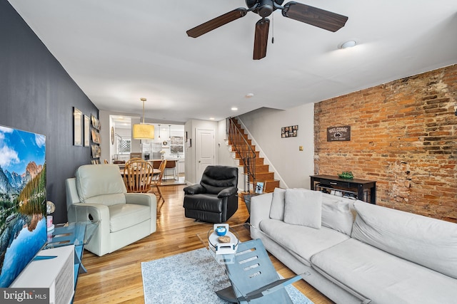 living room with stairway, brick wall, ceiling fan, light wood-style flooring, and a fireplace