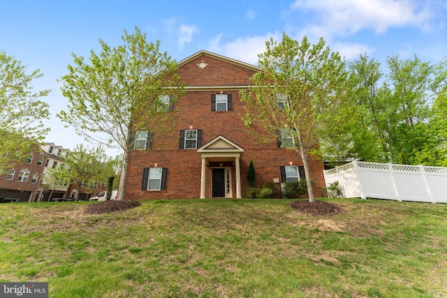 colonial home with brick siding, fence, and a front yard