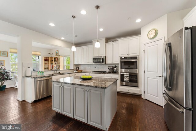 kitchen featuring a center island, appliances with stainless steel finishes, dark wood-type flooring, and a sink