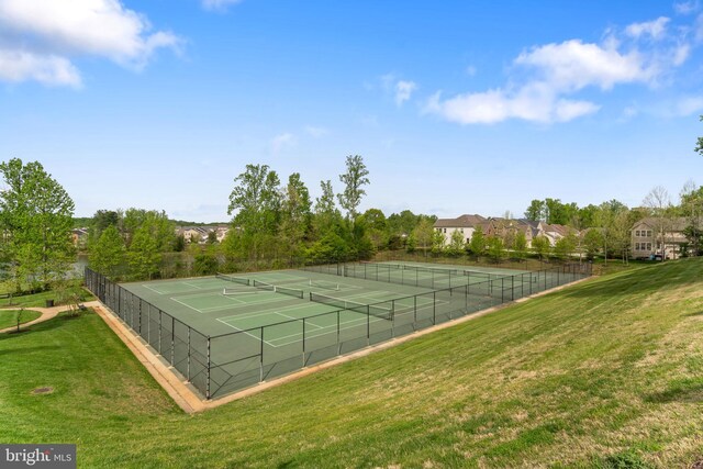view of tennis court with a lawn and fence