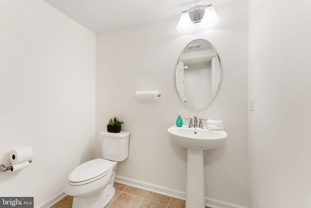 half bath with a sink, toilet, visible vents, baseboards, and tile patterned flooring
