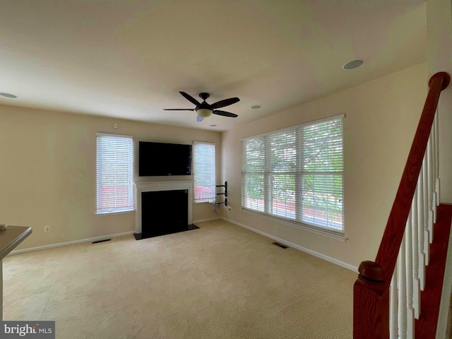 unfurnished living room with visible vents, carpet floors, a ceiling fan, baseboards, and a fireplace with flush hearth