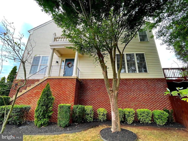 view of front of home featuring stairway, brick siding, and fence