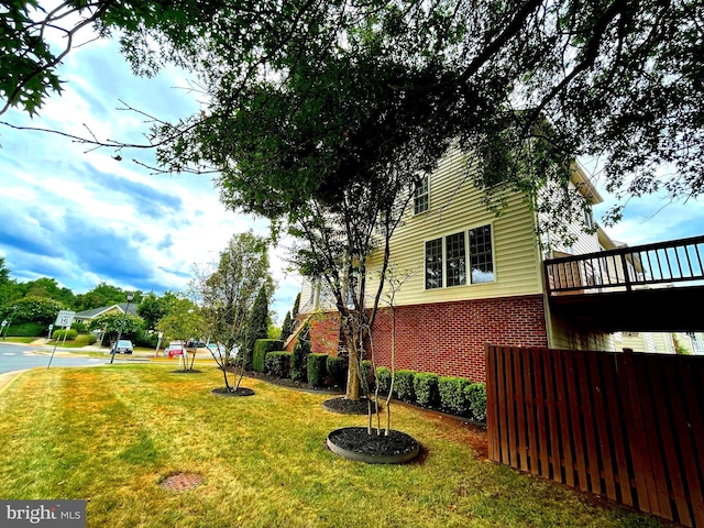 view of side of home featuring a lawn, brick siding, and fence