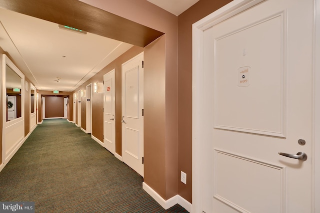 corridor featuring dark colored carpet and baseboards