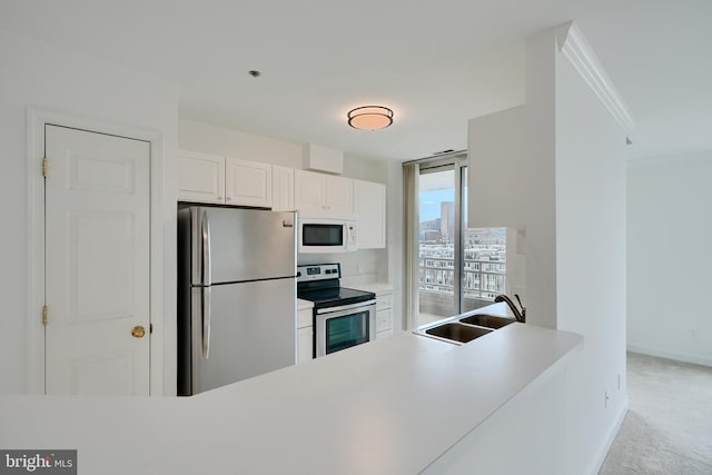 kitchen featuring appliances with stainless steel finishes, a sink, light colored carpet, white cabinetry, and baseboards