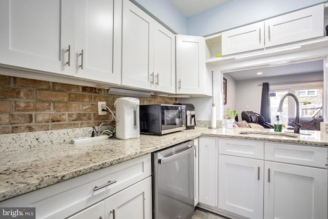kitchen featuring black microwave, white cabinets, light stone countertops, dishwasher, and a sink