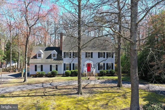colonial house featuring a shingled roof, a front lawn, and a chimney