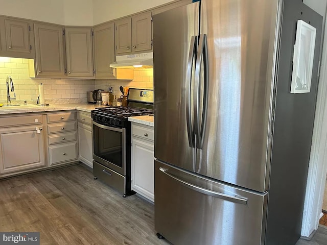 kitchen featuring stainless steel appliances, under cabinet range hood, a sink, light countertops, and tasteful backsplash
