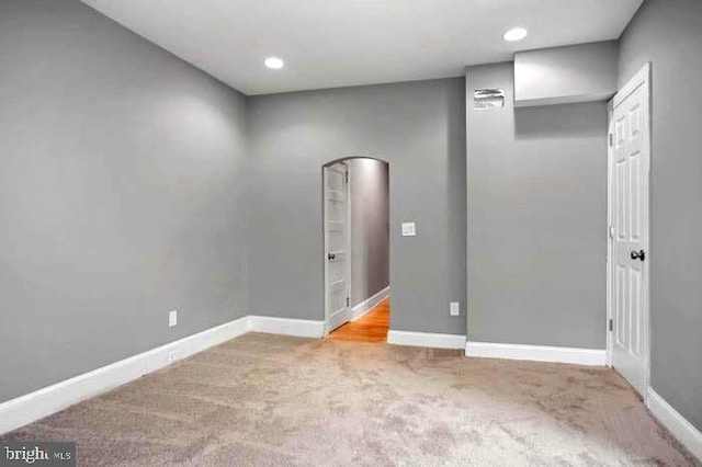 carpeted empty room featuring arched walkways, baseboards, and recessed lighting