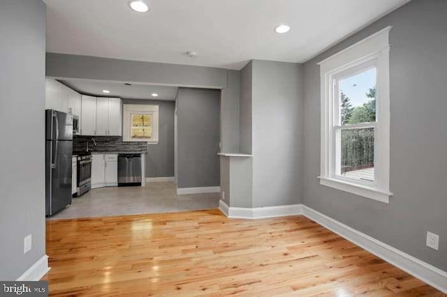 kitchen with tasteful backsplash, stainless steel appliances, baseboards, light wood-style floors, and white cabinets