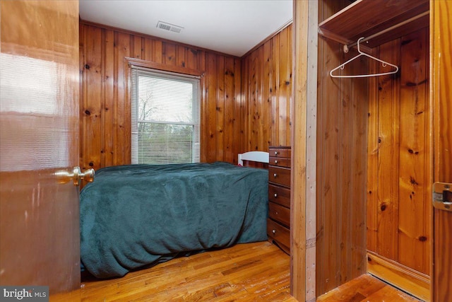 bedroom featuring wooden walls, visible vents, and wood finished floors