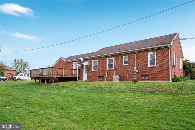 rear view of property with brick siding, a wooden deck, and a yard