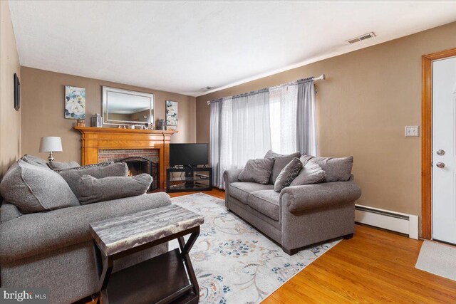 living room featuring baseboard heating, light wood finished floors, a fireplace, and visible vents