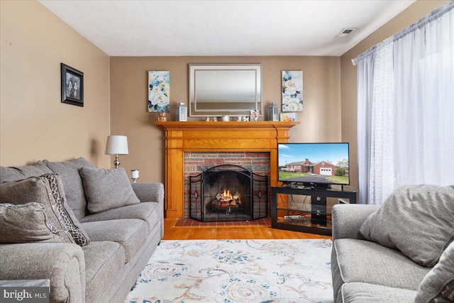 living area with visible vents, a brick fireplace, and wood finished floors