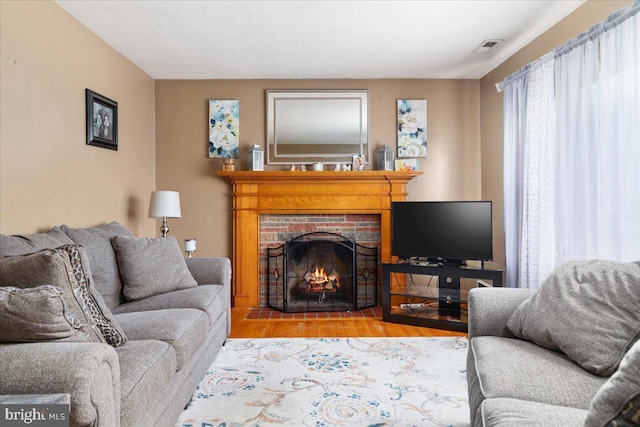 living room with a fireplace with flush hearth, visible vents, and wood finished floors