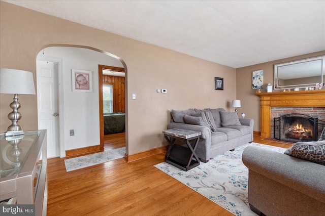 living area featuring a fireplace, arched walkways, light wood-style flooring, and baseboards